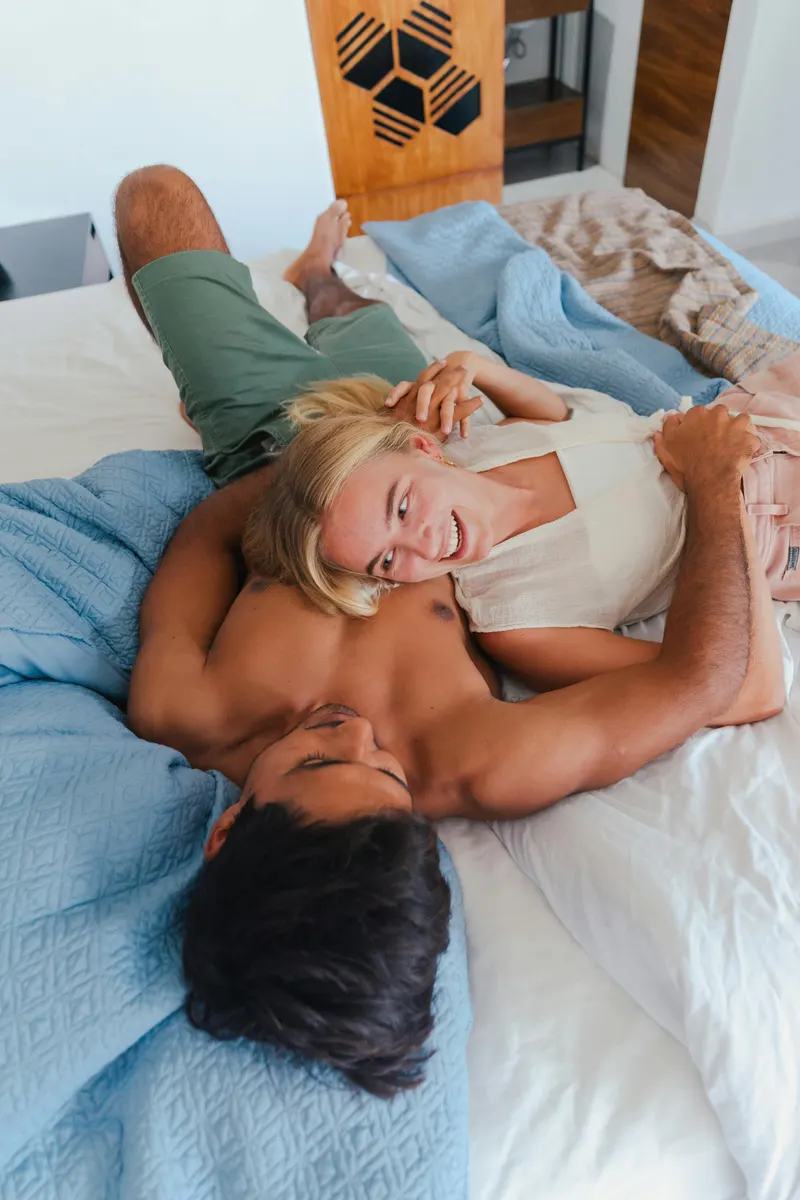 Couple lying in bed together, woman resting on man's chest, smiling, soft blue bedding