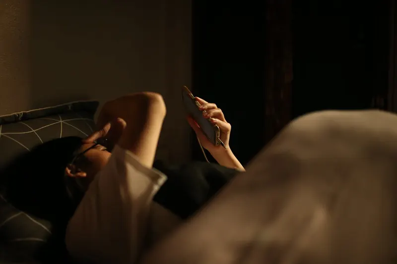 Person lying in bed at night looking at a phone screen, warm ambient lighting