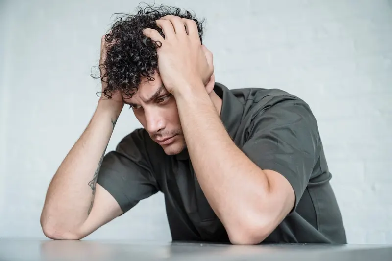 Man sitting with head in hands against a white brick wall, expressing frustration