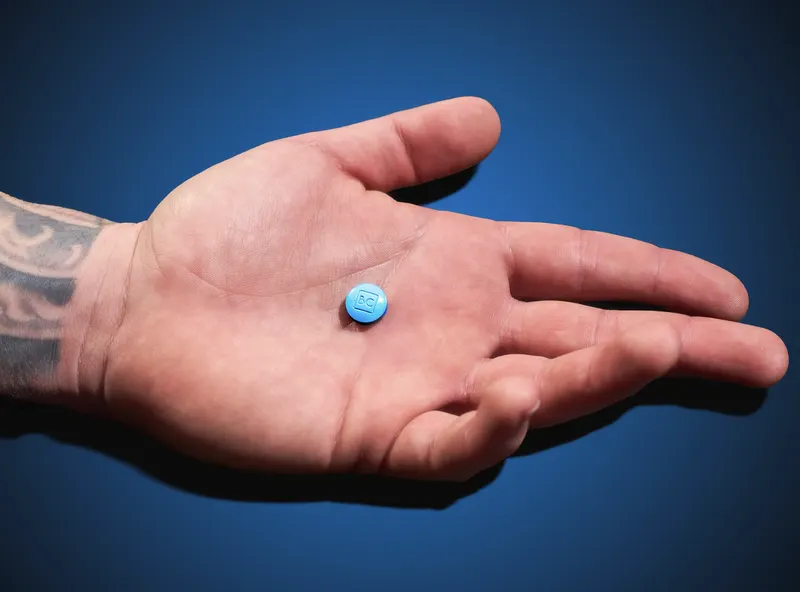 Open palm holding a single blue chewable tablet against a dark blue background, tattoo visible on wrist