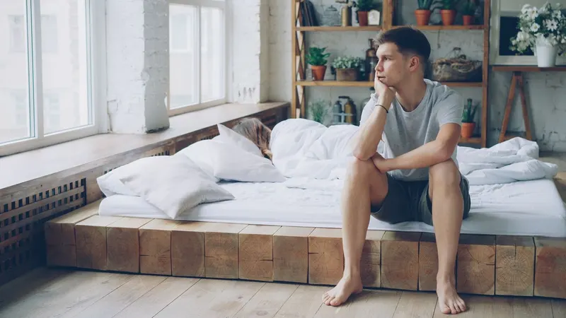 man on bed staring out window depressed