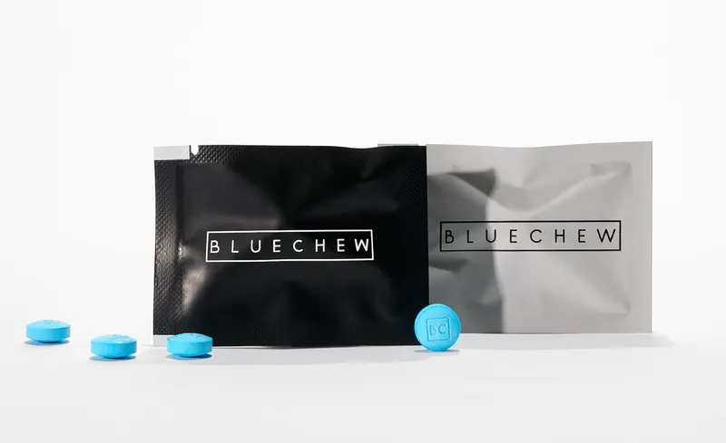 Black and gray BlueChew packets side by side with scattered blue chewable tablets