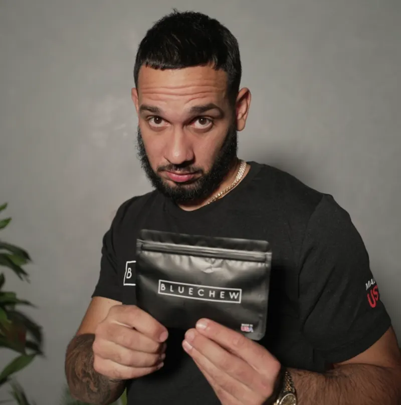 Man in black t-shirt holding an open black BlueChew MAX pouch, looking at the camera