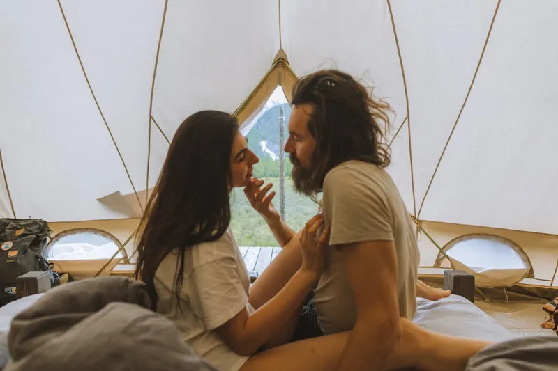 Couple sitting closely together inside a yurt-style tent, touching foreheads affectionately.