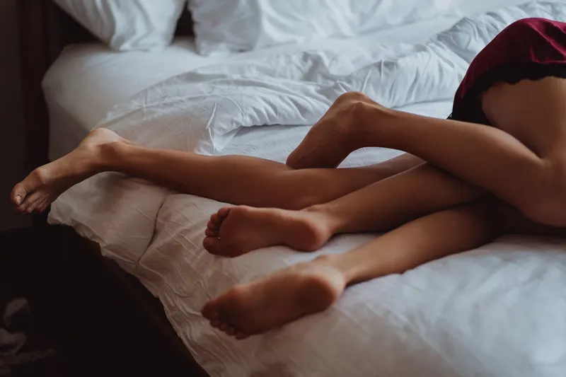 Close-up of two people's tangled legs and feet on a white bed