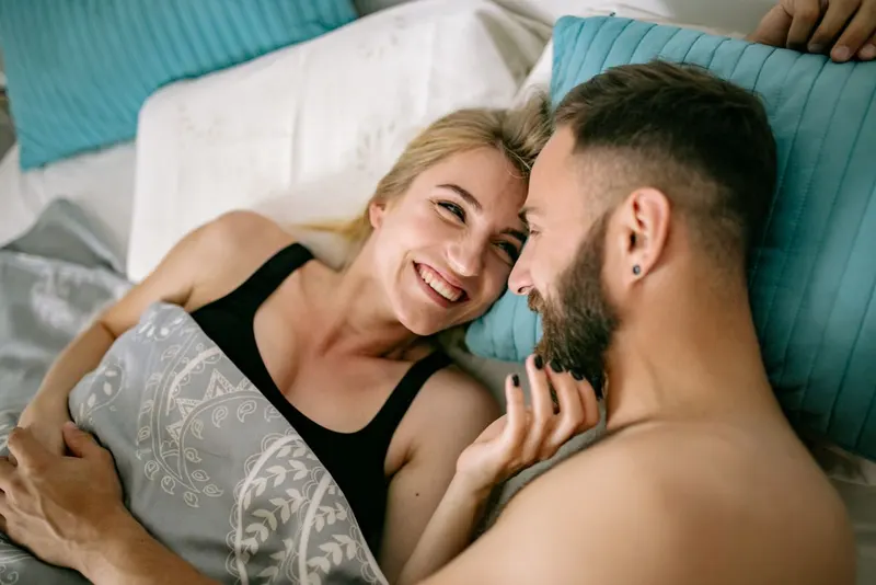 Smiling couple lying in bed together, foreheads touching, embracing.