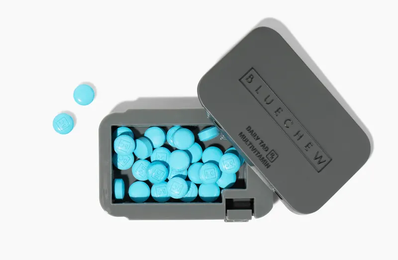 Open gray BlueChew Daily case with loose blue chewable tablets and multivitamin label