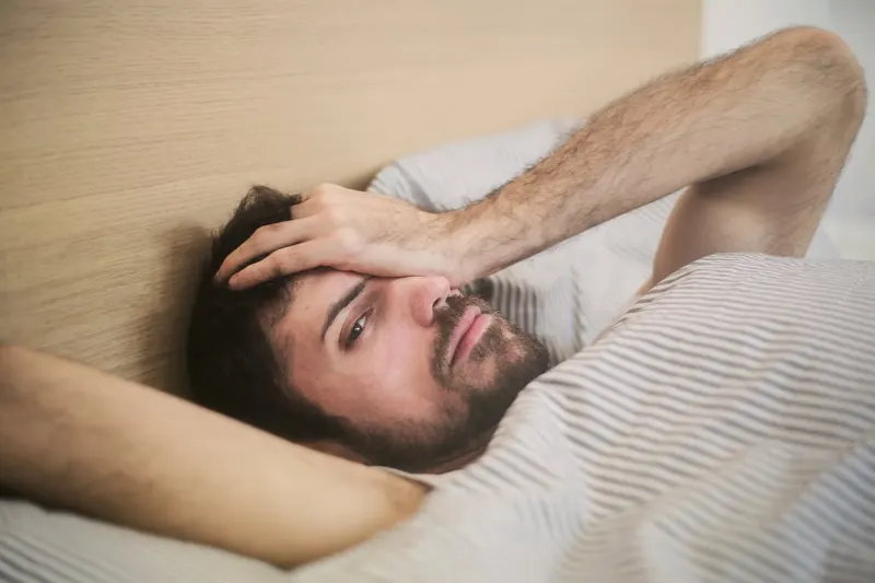 man in bed with hand on his head
