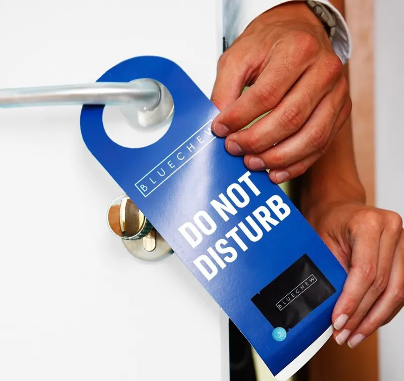 Hand hanging a blue "Do Not Disturb" door hanger branded BlueChew on a door handle.