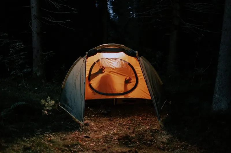 Illuminated tent glowing at night in a dark forest campsite, adventurous outdoor setting