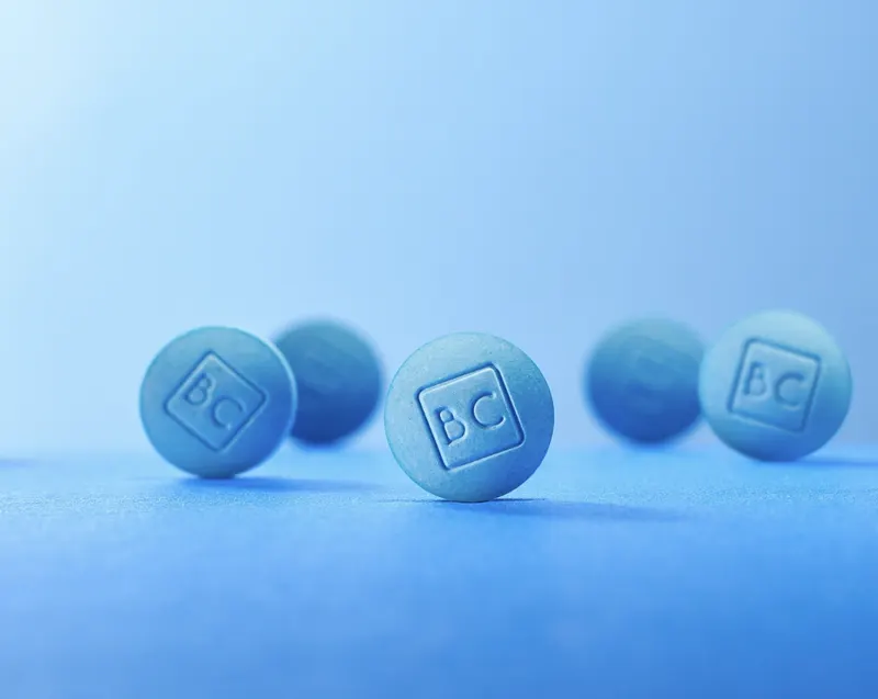 Close-up of blue BlueChew sublingual tablets with 'BC' imprint on a blue surface