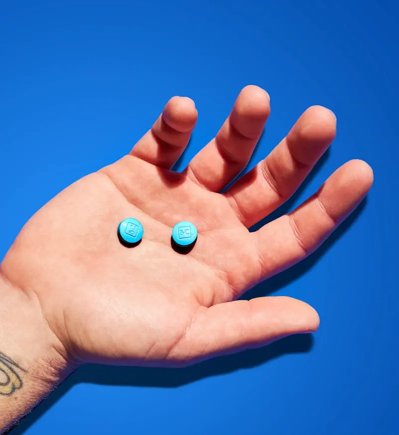 Hand holding two small blue BlueChew tablets against a blue background.