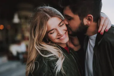 Smiling couple embracing warmly, man kissing woman's cheek, cozy indoor setting