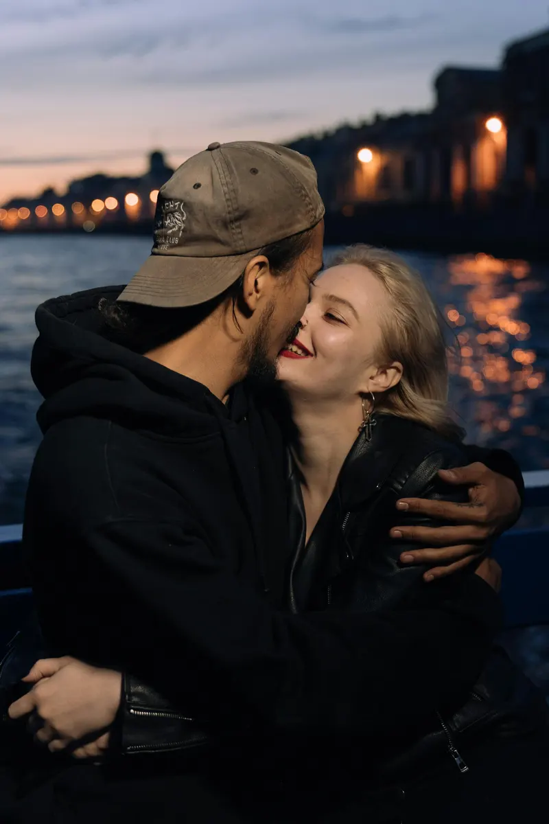 Couple embracing closely at dusk on a waterfront, city lights in the background