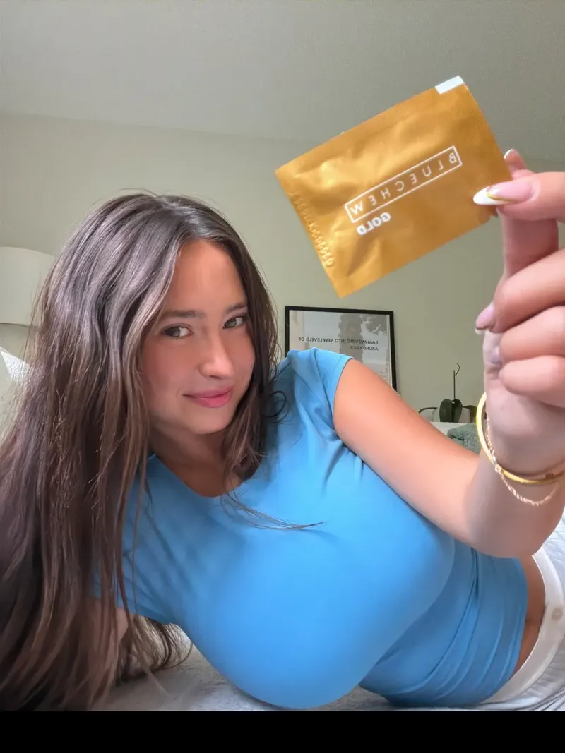 Woman in a blue top holding up a gold BlueChew GOLD sachet